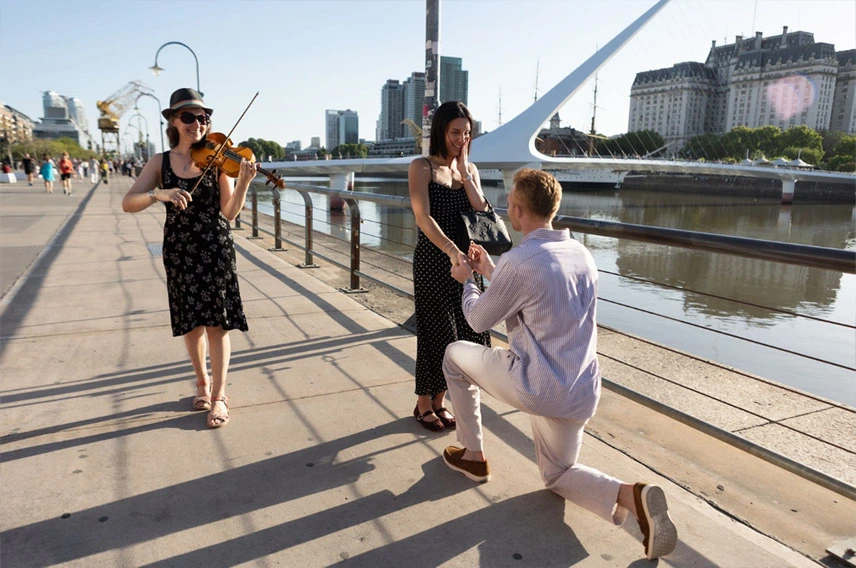 Groom proposing in Puerto Madero while a violinist plays during a surprise proposal in Buenos Aires.
